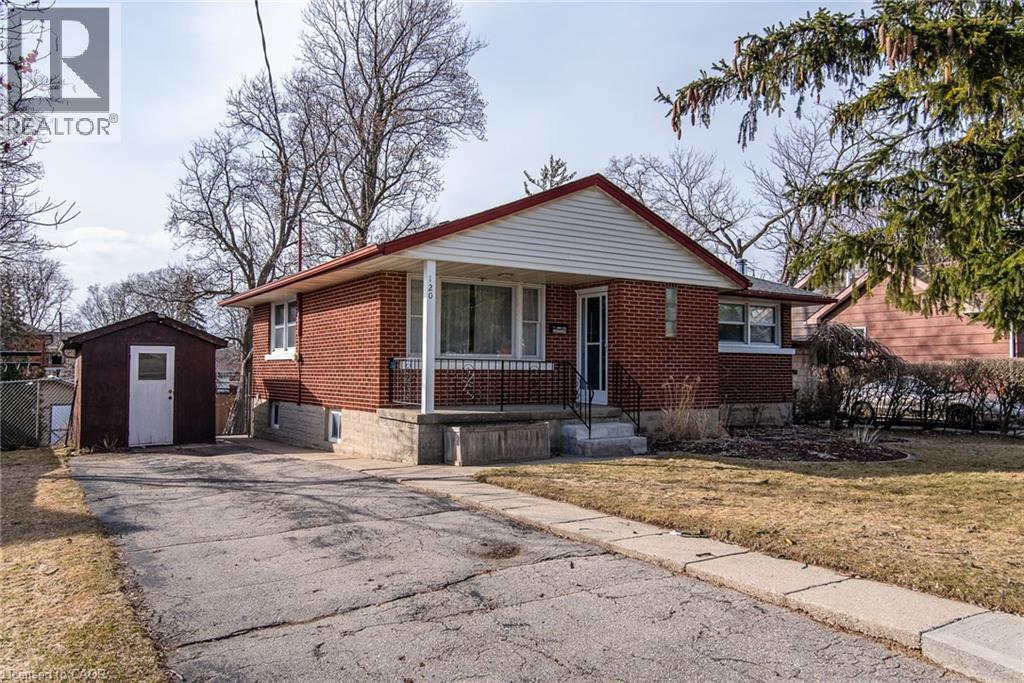 Bungalow-style house featuring brick siding, a storage unit, asphalt driveway, a porch, and a front lawn - 120 Fourth Avenue, Kitchener, ON - Outdoor