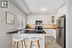 Kitchen with stainless steel appliances, a peninsula, a breakfast bar area, dark stone countertops, and white cabinetry -