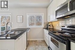 Kitchen with appliances with stainless steel finishes, white cabinets, dark stone counters, and backsplash -