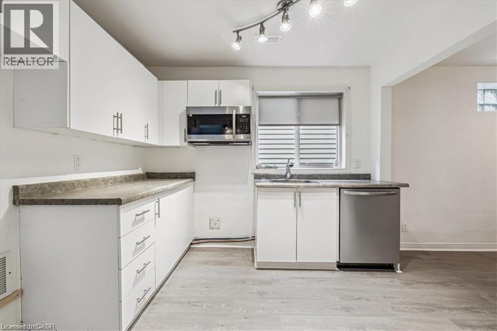 Kitchen featuring appliances with stainless steel finishes, white cabinets, light wood finished floors, and dark countertops - 28 Grove Street, Hamilton, ON - Indoor Photo Showing Kitchen
