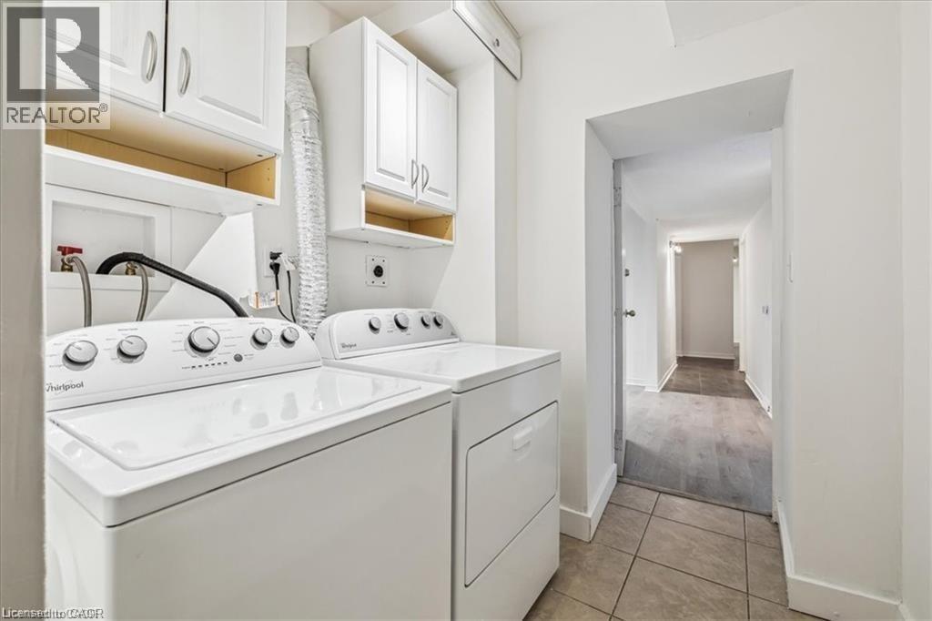 Laundry room with washing machine and dryer, cabinet space, and light tile patterned floors - 28 Grove Street, Hamilton, ON - Indoor Photo Showing Laundry Room