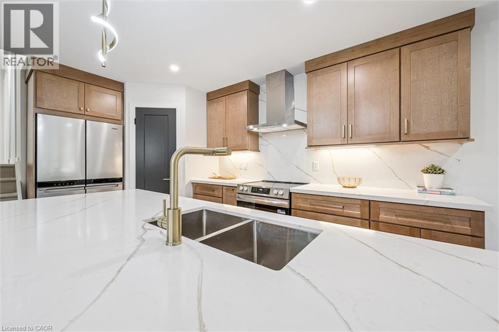 Kitchen featuring wall chimney exhaust hood, stainless steel appliances, light stone countertops, brown cabinetry, and recessed lighting - 459 Drummerhill Crescent, Waterloo, ON - Indoor Photo Showing Kitchen With Stainless Steel Kitchen With Double Sink With Upgraded Kitchen