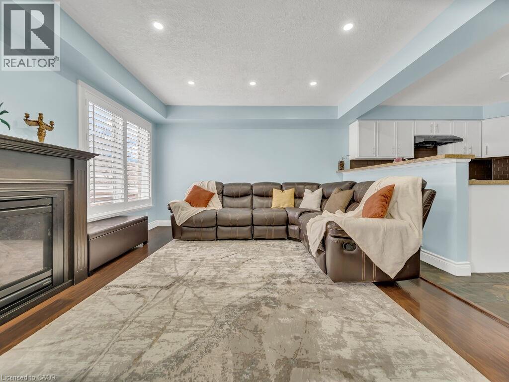 Living room with a tray ceiling, recessed lighting, dark wood-type flooring, a textured ceiling, and a glass covered fireplace - 29 Amsterdam Crescent, Guelph, ON - Indoor Photo Showing Living Room With Fireplace