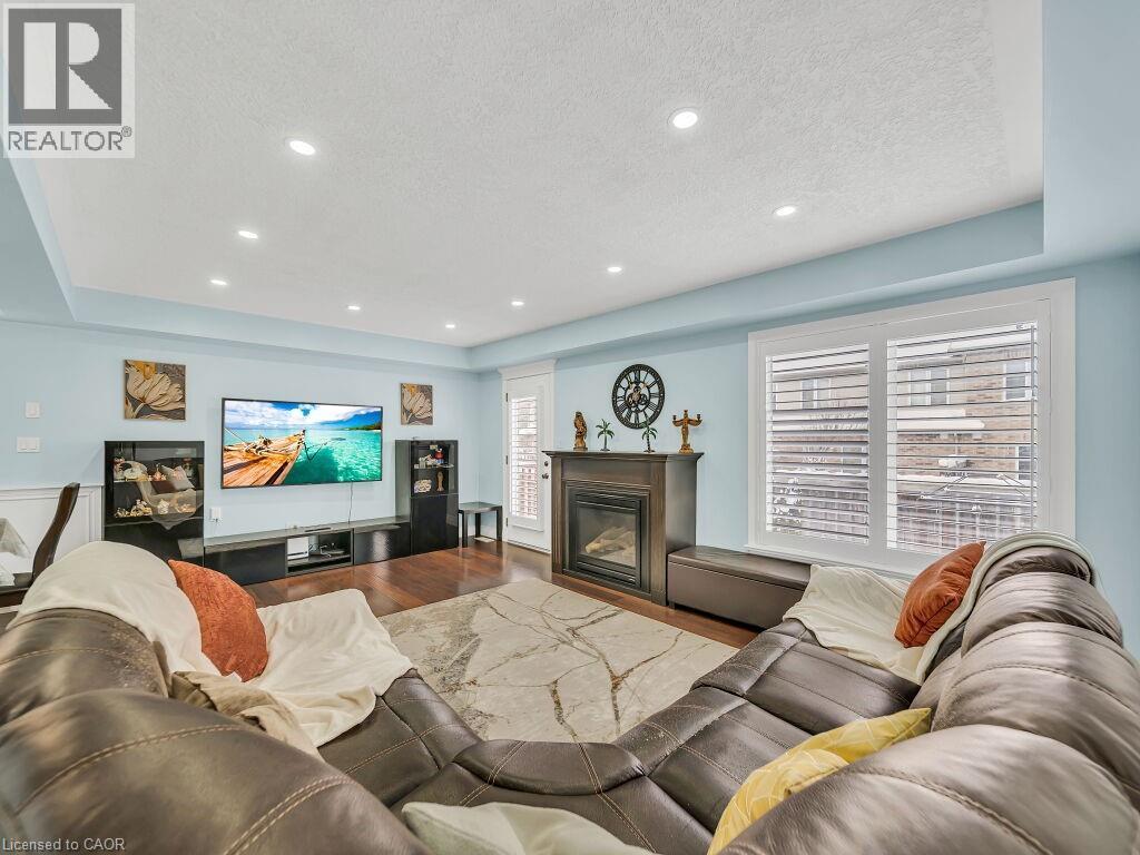 Living area featuring a raised ceiling, a glass covered fireplace, wood finished floors, a textured ceiling, and recessed lighting - 29 Amsterdam Crescent, Guelph, ON - Indoor Photo Showing Living Room With Fireplace