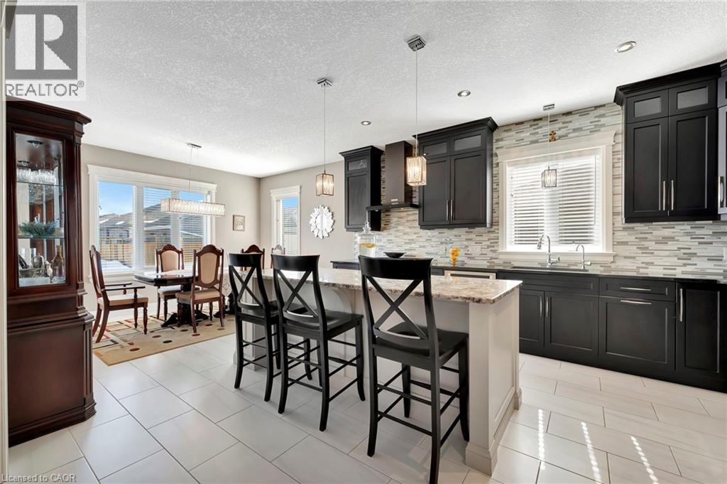 Kitchen with a kitchen breakfast bar, decorative light fixtures, light stone countertops, a center island, and a textured ceiling - 107 Forbes Crescent, Listowel, ON - Indoor