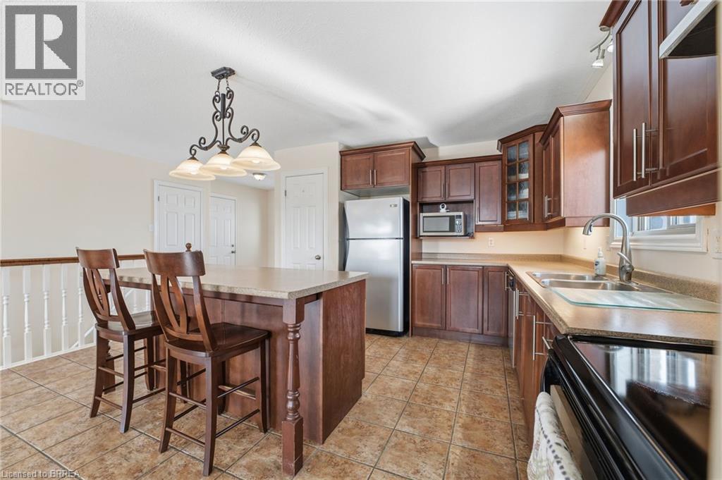 Kitchen with stainless steel appliances, glass insert cabinets, pendant lighting, a center island, and a kitchen breakfast bar - 28 Mansfield Drive, St. George, ON - Indoor Photo Showing Kitchen With Double Sink