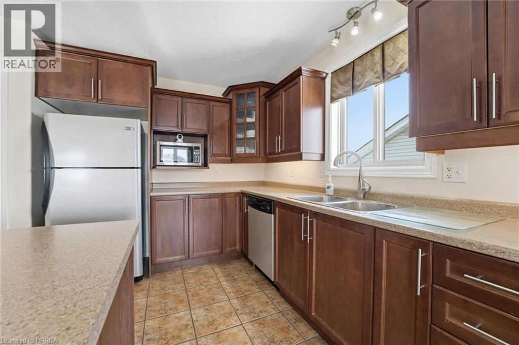 Kitchen featuring glass insert cabinets, stainless steel appliances, and dark brown cabinetry - 28 Mansfield Drive, St. George, ON - Indoor Photo Showing Kitchen With Double Sink