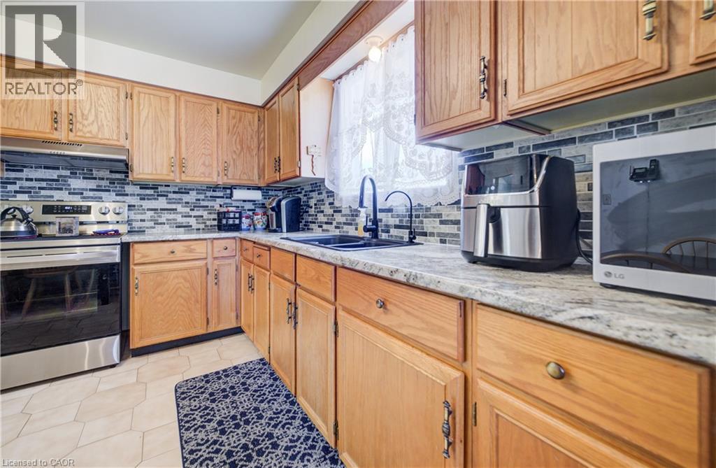 Kitchen with stainless steel appliances, under cabinet range hood, light stone countertops, and backsplash - 42 Ruffian Road, Brantford, ON - Indoor Photo Showing Kitchen With Double Sink