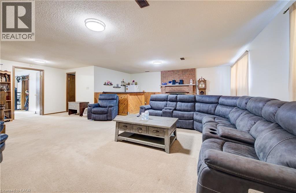 Carpeted recreation room featuring a textured ceiling and a brick fireplace - 42 Ruffian Road, Brantford, ON - Indoor Photo Showing Living Room