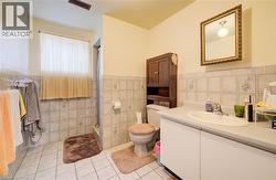 Bathroom with vanity, a shower stall, a wainscoted wall, light tile patterned floors, and tile walls -
