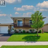 Split level home featuring a balcony, brick siding, a front yard, a garage, and driveway -