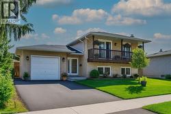 Split level home with an attached garage, a front yard, asphalt driveway, and a balcony -