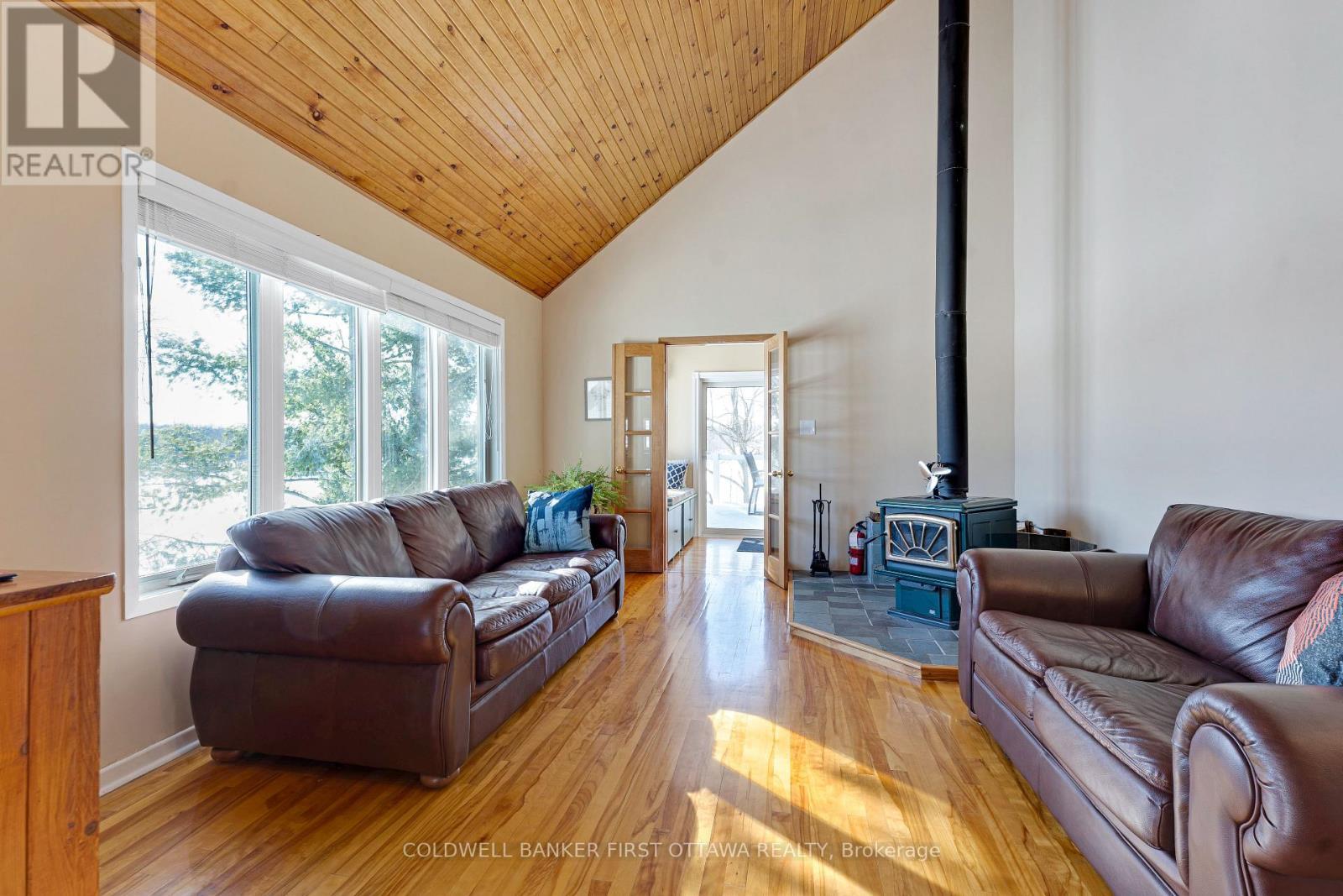 Familyroom woodstove & wall of windows facing lake - 100 Nagle Way, Tay Valley, ON - Indoor Photo Showing Living Room