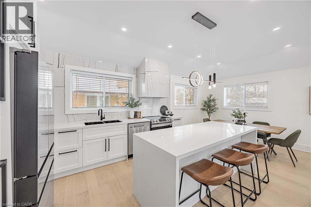 Kitchen featuring white cabinetry, a breakfast bar area, light wood-style flooring, appliances with stainless steel finishes, and light stone counters - 248 Wales Crescent, Oakville, ON - Indoor Photo Showing Kitchen With Double Sink With Upgraded Kitchen
