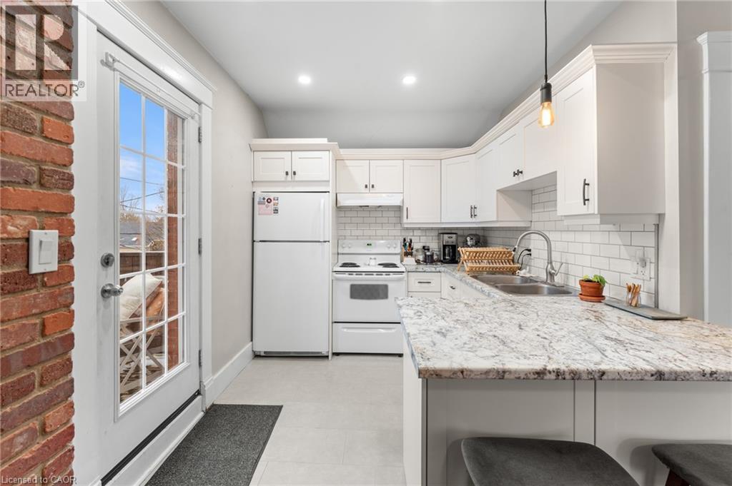 Kitchen with white appliances, white cabinetry, a breakfast bar area, backsplash, and decorative light fixtures - 58 Hohner Avenue, Kitchener, ON - Indoor Photo Showing Kitchen With Double Sink