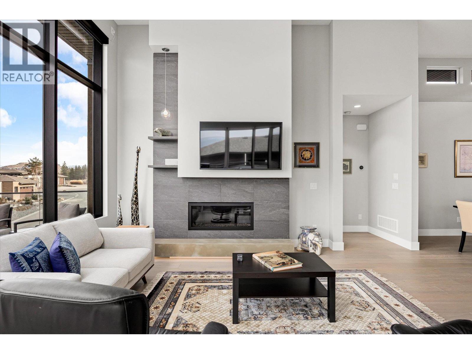 A cozy gas fireplace with a floor to ceiling tile surround and moody under lighting - 468 Sparrow Hawk Court, Kelowna, BC - Indoor Photo Showing Living Room With Fireplace