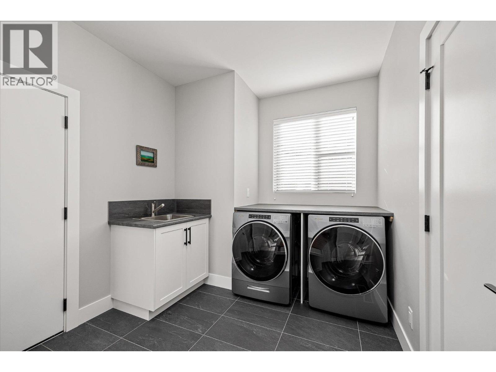 Laundry/Mud room featuring an Arborite counter, stainless steel sink, Whirlpool washer and dryer and a bright window overlooking the front yard - 468 Sparrow Hawk Court, Kelowna, BC - Indoor Photo Showing Laundry Room