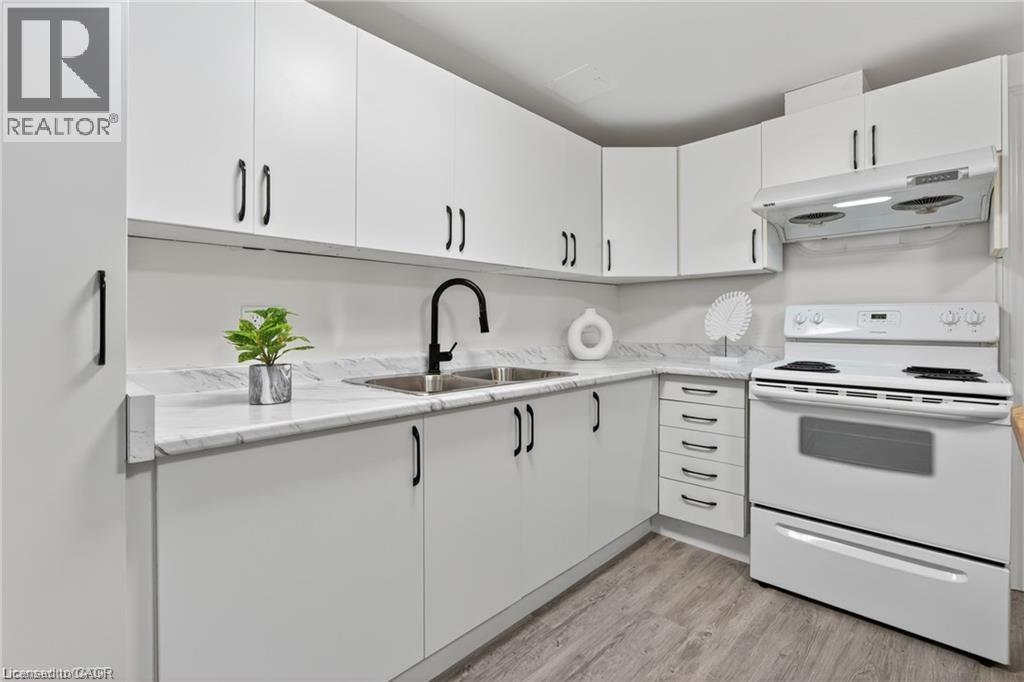 Kitchen with white range with electric stovetop, under cabinet range hood, light wood finished floors, and white cabinets - 146 Appalachian Crescent Unit# Lower, Kitchener, ON - Indoor Photo Showing Kitchen With Double Sink