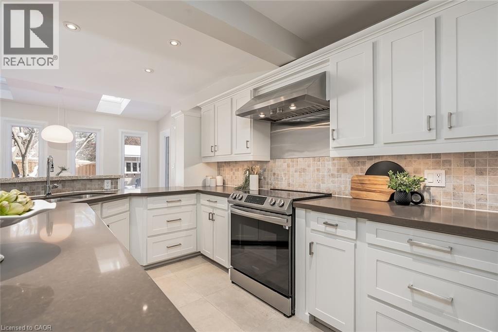 Kitchen featuring electric stove, hanging light fixtures, wall chimney exhaust hood, a skylight, and white cabinets - 4226 Dunvegan Road, Burlington, ON - Indoor Photo Showing Kitchen With Upgraded Kitchen