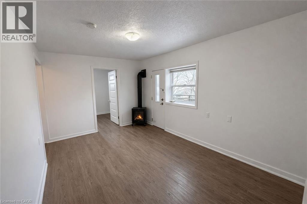 Unfurnished bedroom with a walk in closet, dark wood finished floors, a textured ceiling, and a wood stove - 46 College Street, Kitchener, ON - Indoor Photo Showing Other Room