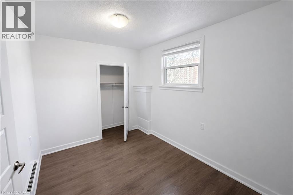 Unfurnished bedroom with dark wood-style flooring, a textured ceiling, a closet, and baseboard heating - 46 College Street, Kitchener, ON - Indoor Photo Showing Other Room
