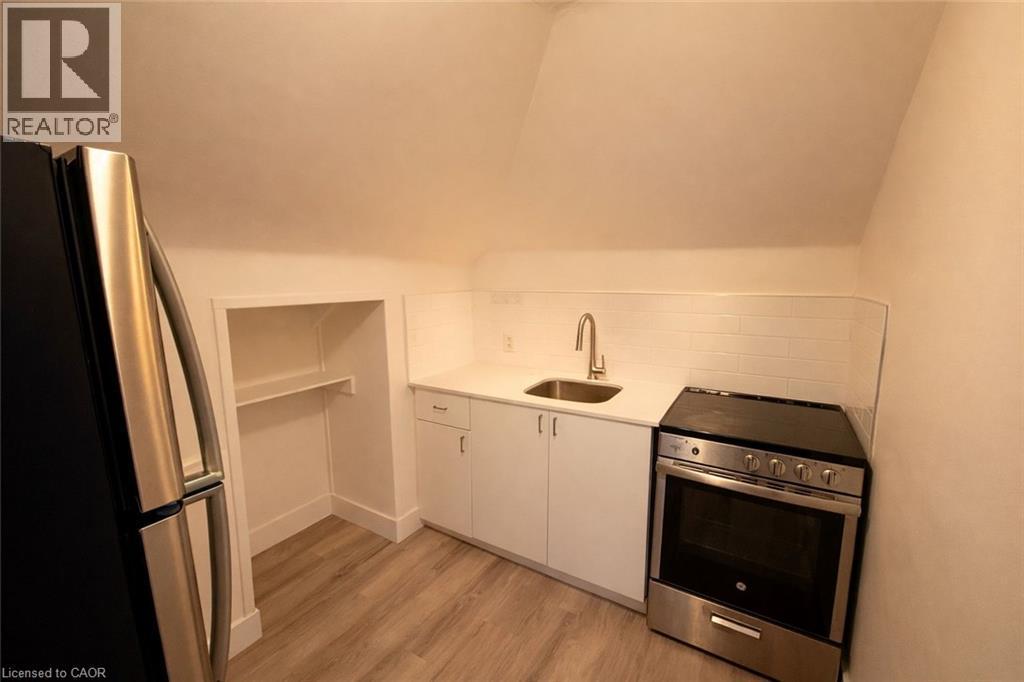 Kitchen featuring appliances with stainless steel finishes, white cabinetry, light wood-style flooring, light stone counters, and decorative backsplash - 44 Weber Street W, Kitchener, ON - Indoor Photo Showing Kitchen