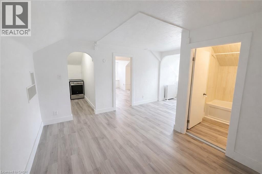 Unfurnished living room featuring light wood-type flooring, arched walkways, and radiator heating unit - 44 Weber Street W, Kitchener, ON - Indoor Photo Showing Other Room