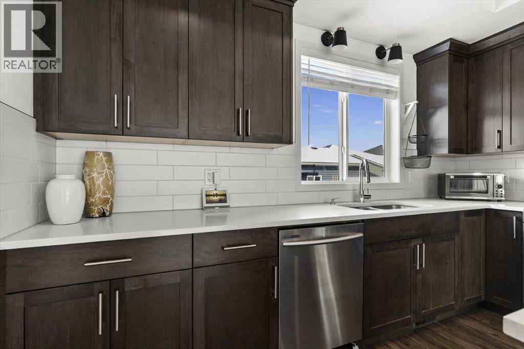Gleaming quartz counters and designer influenced subway tile backsplash highlight this functional space - 59 Wolf Hollow Way Se, Calgary, AB - Indoor Photo Showing Kitchen With Double Sink