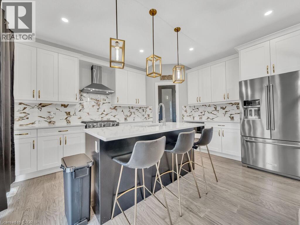 Kitchen with high quality fridge, white cabinetry, decorative light fixtures, an island with sink, and recessed lighting - 3374 Oriole Drive, London, ON - Indoor Photo Showing Kitchen With Upgraded Kitchen