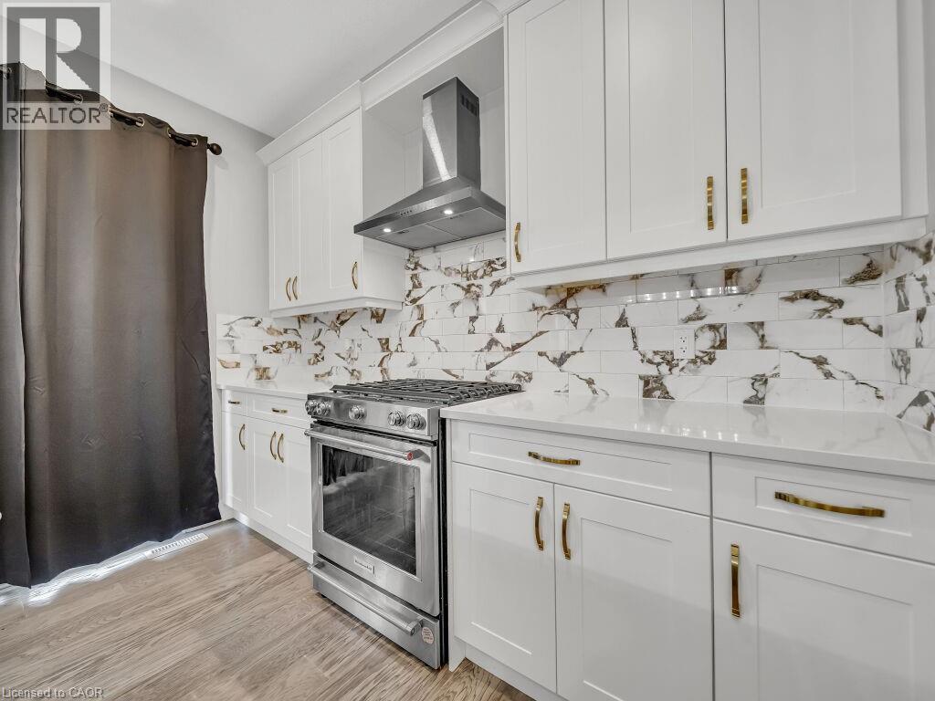 Kitchen featuring white cabinetry, wall chimney exhaust hood, gas range, light stone counters, and light wood-style floors - 3374 Oriole Drive, London, ON - Indoor Photo Showing Kitchen