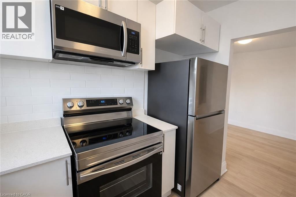Kitchen featuring stainless steel appliances, white cabinets, light wood-type flooring, light stone countertops, and backsplash - 17 Louisa Street, Kitchener, ON - Indoor Photo Showing Kitchen