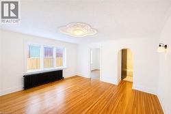Empty room featuring radiator heating unit, arched walkways, light wood-type flooring, and a textured ceiling -