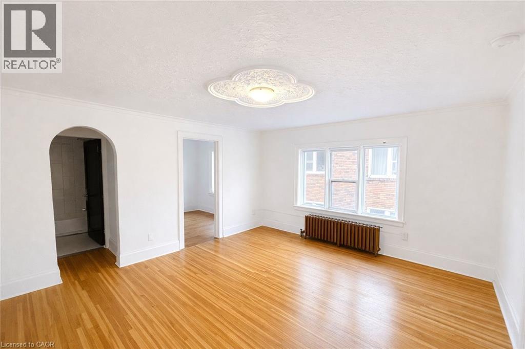 Spare room with radiator, arched walkways, light wood-type flooring, a textured ceiling, and ornamental molding - 112 Margaret Avenue, Kitchener, ON - Indoor Photo Showing Other Room