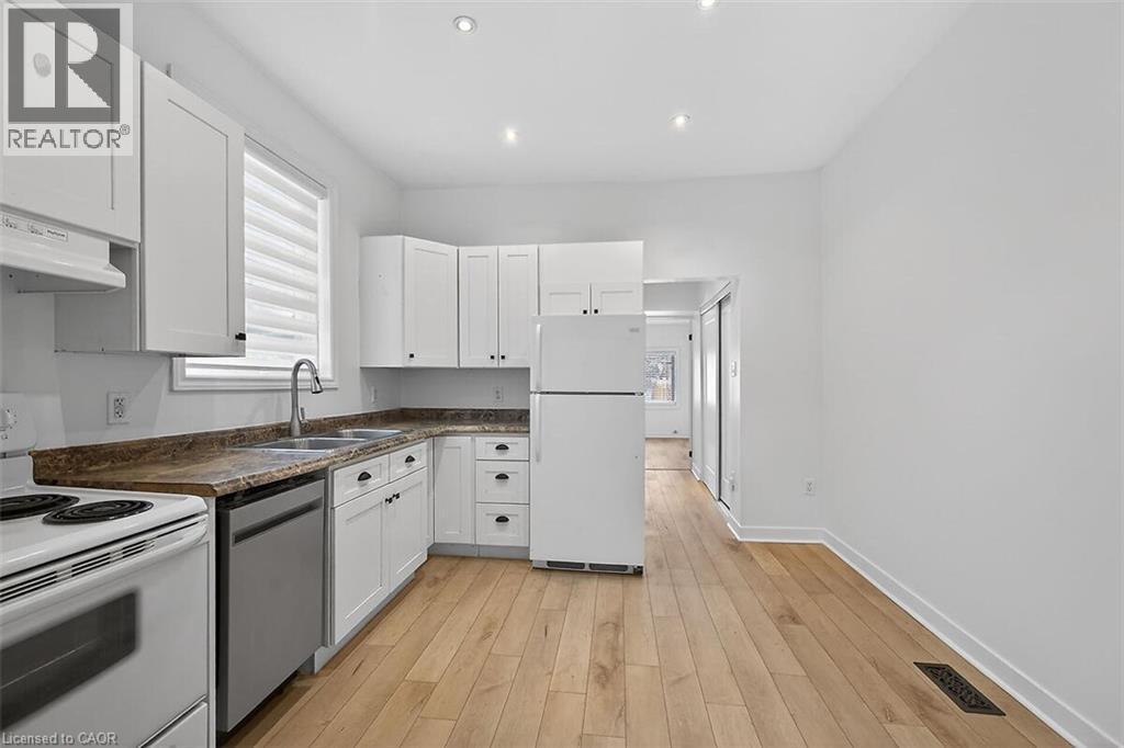 Kitchen with dark countertops, white appliances, white cabinets, light wood-style flooring, and recessed lighting - 77 Barton Street E Unit# 1, Hamilton, ON - Indoor Photo Showing Kitchen With Double Sink