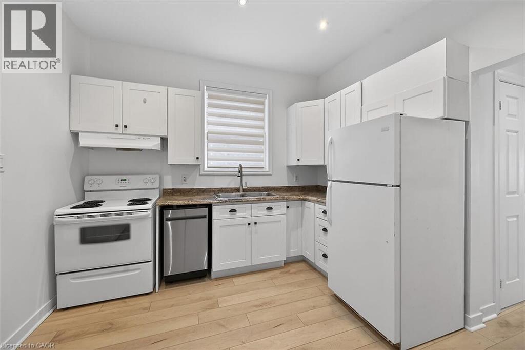 Kitchen featuring white appliances, white cabinets, light wood-style flooring, and under cabinet range hood - 77 Barton Street E Unit# 1, Hamilton, ON - Indoor Photo Showing Kitchen