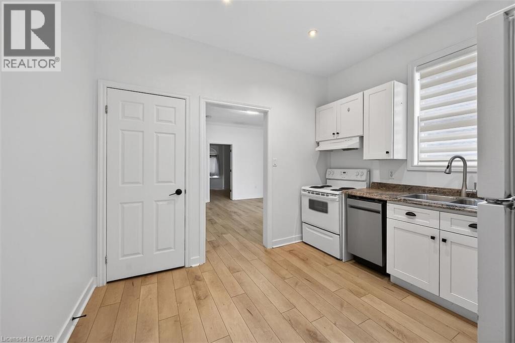 Kitchen featuring white cabinets, white appliances, light wood-type flooring, dark stone counters, and under cabinet range hood - 77 Barton Street E Unit# 1, Hamilton, ON - Indoor Photo Showing Kitchen