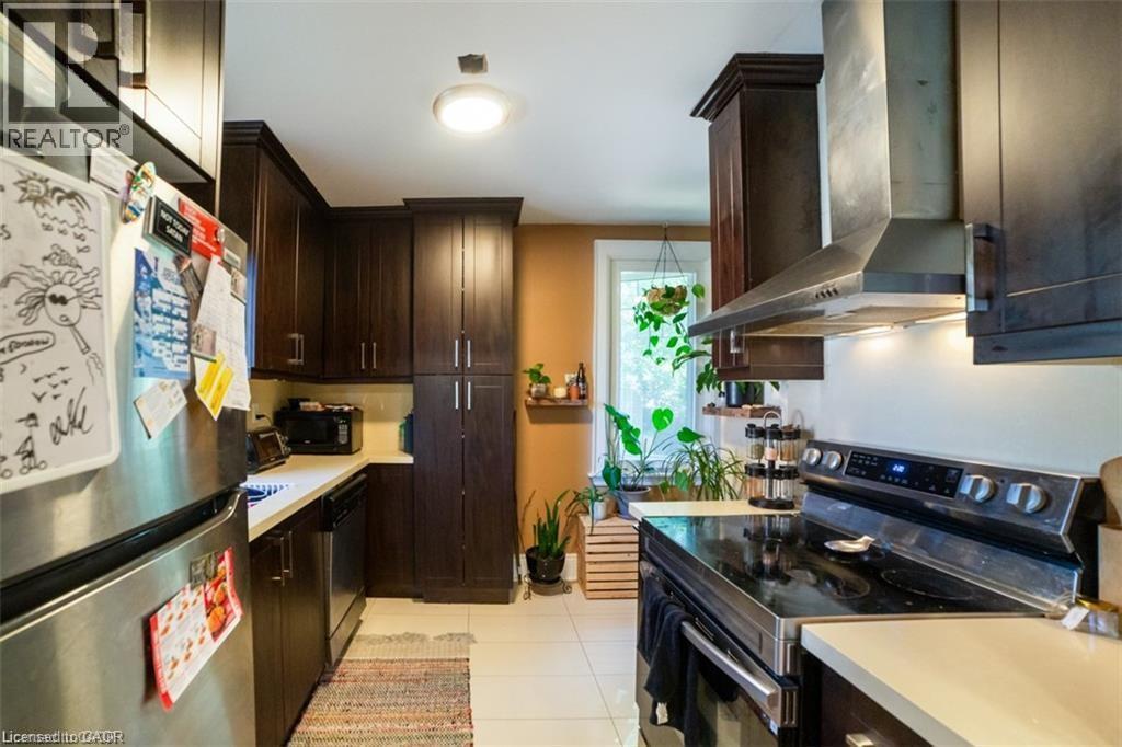 Kitchen featuring appliances with stainless steel finishes, dark brown cabinets, wall chimney range hood, light countertops, and light tile patterned floors - 41 Paradise Road S, Hamilton, ON - Indoor Photo Showing Kitchen