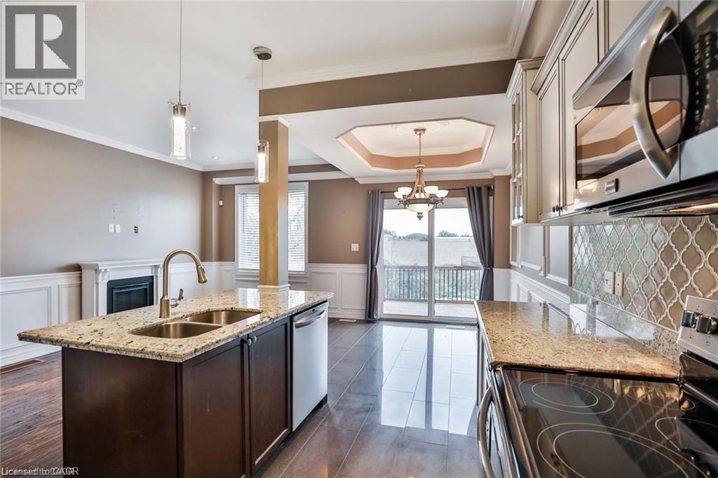 Kitchen featuring stainless steel appliances, light stone countertops, an island with sink, dark wood-style flooring, and a wainscoted wall - 42 Madonna Drive, Hamilton, ON - Indoor Photo Showing Kitchen With Double Sink