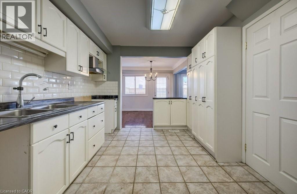 Kitchen featuring dark countertops, a chandelier, backsplash, pendant lighting, and white cabinets - 54 Nicklaus Drive, Hamilton, ON - Indoor Photo Showing Kitchen With Double Sink