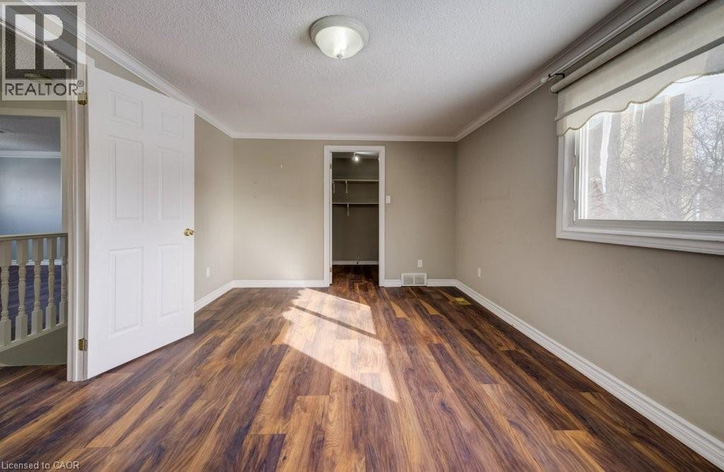 Unfurnished bedroom with dark wood-type flooring, a spacious closet, crown molding, and a textured ceiling - 54 Nicklaus Drive, Hamilton, ON - Indoor Photo Showing Other Room