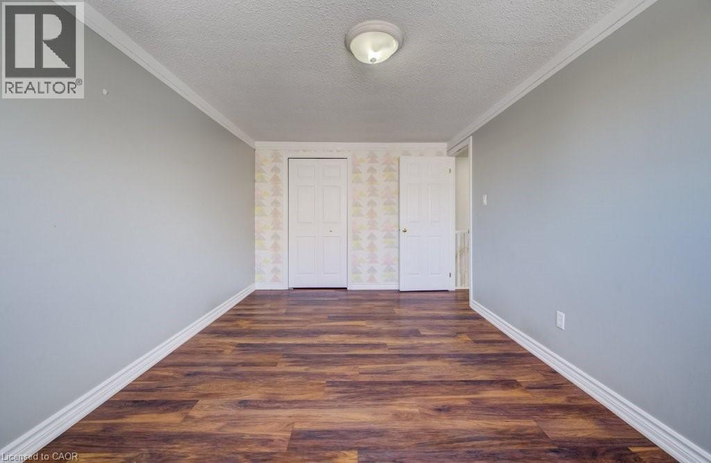 Unfurnished bedroom with dark wood-style floors, a textured ceiling, crown molding, a closet, and wallpapered walls - 54 Nicklaus Drive, Hamilton, ON - Indoor Photo Showing Other Room