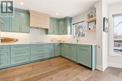 Kitchen with green cabinets, custom range hood, open shelves, light wood-style flooring, and backsplash -