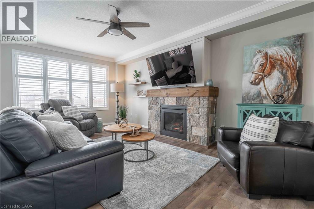 Living area with a beautiful stone fireplace complete with ornamental molding, wood finished floors, and a ceiling fan - 115 Larry Crescent, Caledonia, ON - Indoor Photo Showing Living Room With Fireplace