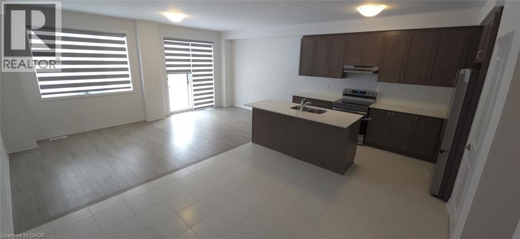 Kitchen featuring light countertops, dark brown cabinetry, freestanding refrigerator, electric range oven, and a kitchen island with sink - 925 Douro Street, Stratford, ON - Indoor Photo Showing Kitchen With Double Sink