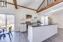 Kitchen featuring appliances with stainless steel finishes, dark countertops, high vaulted ceiling, white cabinetry, and baseboards -