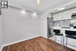 Kitchen featuring light countertops, freestanding refrigerator, backsplash, white cabinets, and wood finished floors -