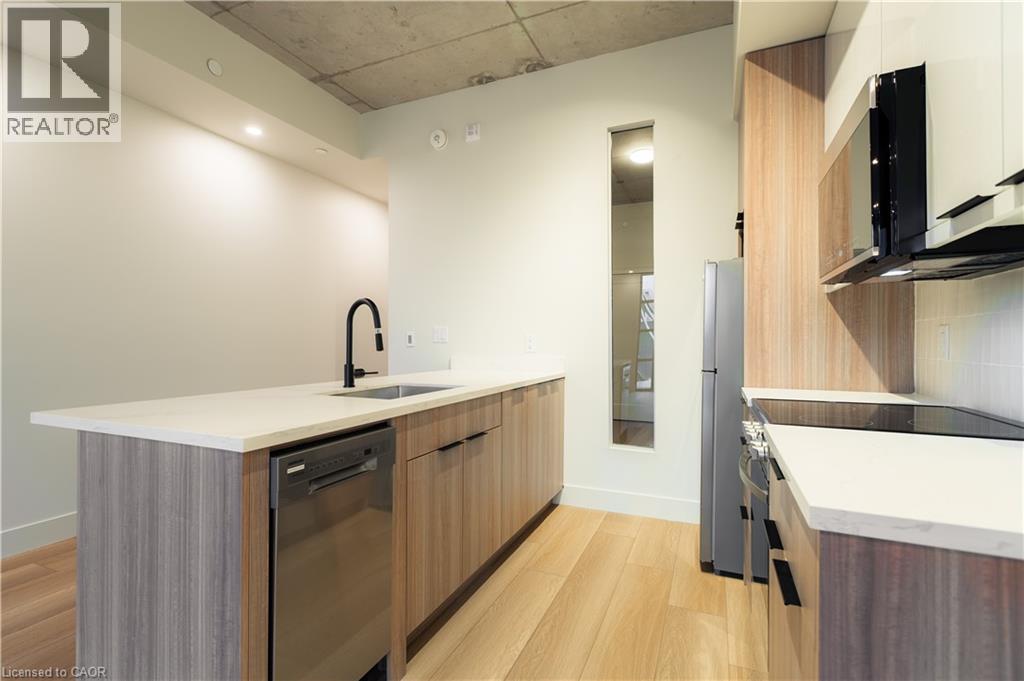 Kitchen with modern cabinets, stainless steel appliances, a peninsula, light stone counters, and light wood-style floors - 24 Augusta Street Unit# 305, Hamilton, ON - Indoor Photo Showing Kitchen