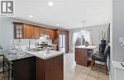 Kitchen with a peninsula, stainless steel appliances, brown cabinetry, hanging light fixtures, and light tile patterned floors -