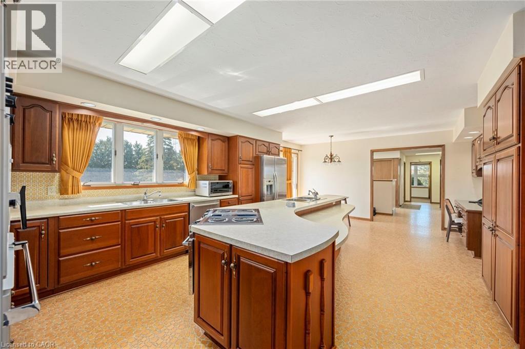 Kitchen with light floors, brown cabinets, light countertops, a center island with sink, and stainless steel appliances - 6828 Third Line, Chatham, ON