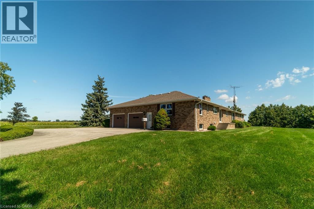 View of side of property featuring concrete driveway, brick siding, a lawn, a chimney, and an attached garage - 6828 Third Line, Chatham, ON